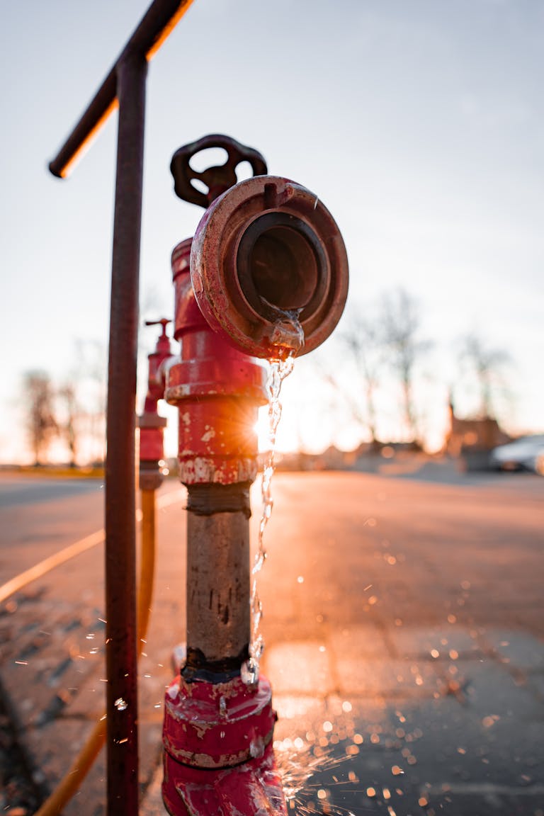 A rusty fire hydrant with water drops at sunset on a pavement.